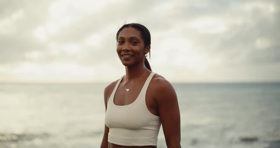 Slow motion portrait of a serene athletic woman on a cloudy beach who opens her eyes and smiles warmly at the camera