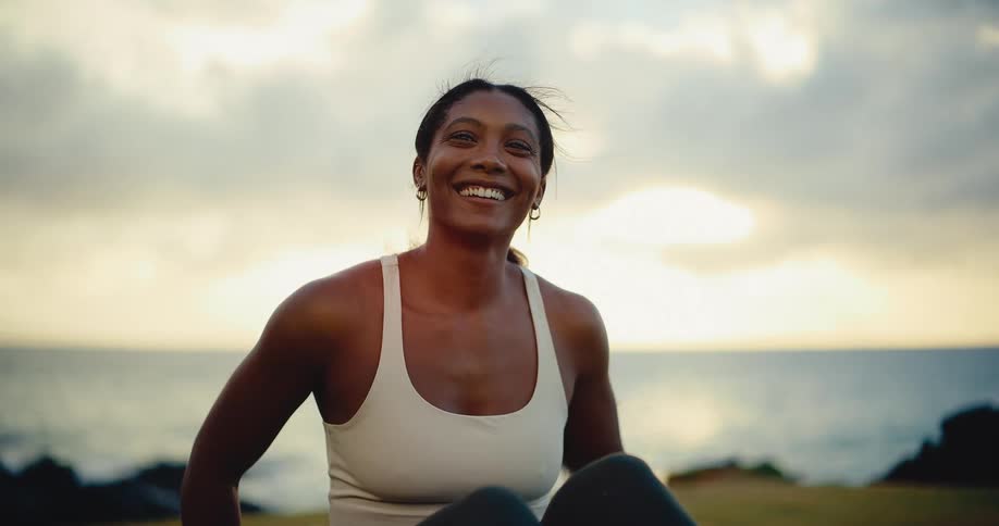 Slow motion portrait of a beautiful and athletic woman smiling peacefully by the ocean at sunset after a workout