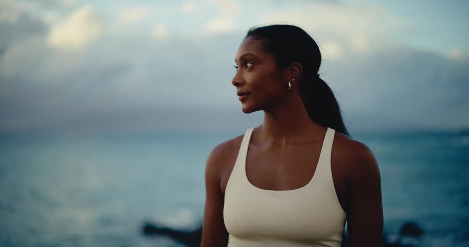 Slow motion portrait of a calm and beautiful young woman enjoying a peaceful moment by the ocean at sunset
