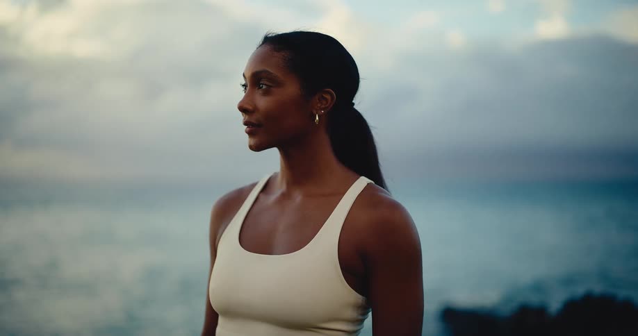Slow motion close-up of a beautiful athletic woman looking serenely out at the ocean at sunrise