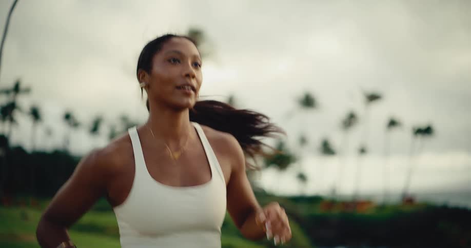 A fit woman jogs outdoors in slow motion through a beautiful tropical park with palm trees