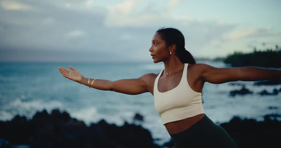 Slow motion shot of a mindful woman transitioning through yoga poses on a beautiful rocky coastline