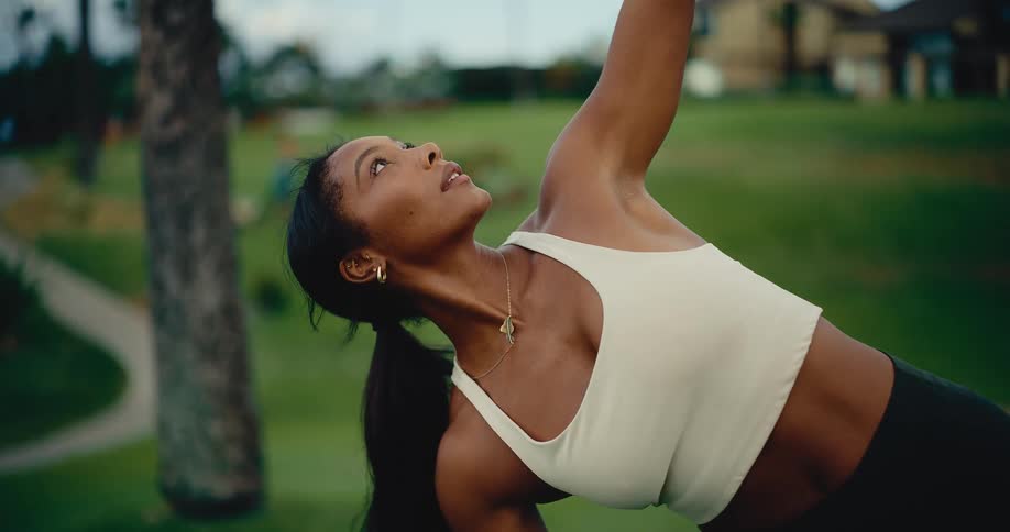 A beautiful and strong woman gracefully holds a yoga pose in a tranquil seaside park, embodying health and wellness