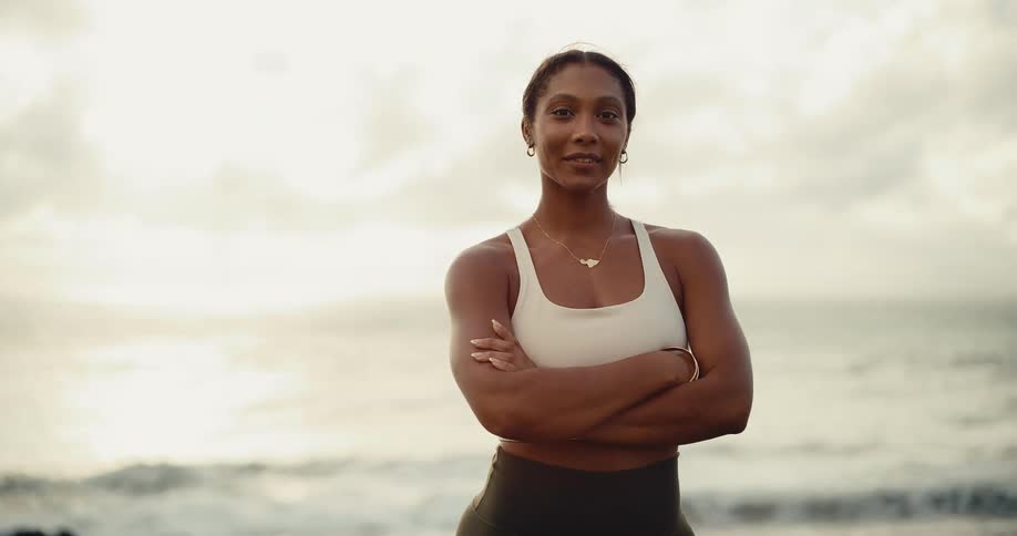 A confident and strong athletic woman smiles at the camera while standing on a tropical beach at sunrise