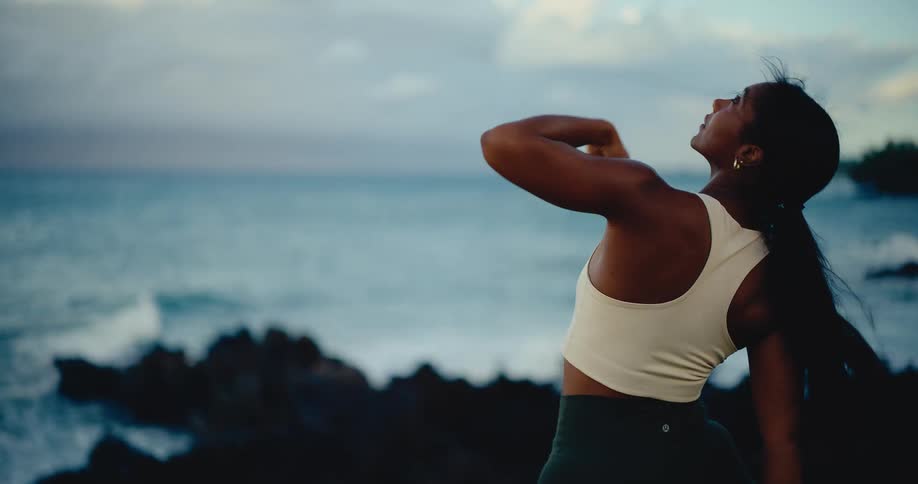 A graceful woman in a serene yoga flow on a grassy cliff overlooking the ocean at dawn