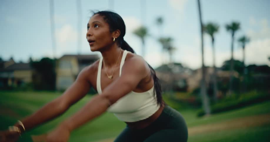 A strong and serene woman transitions from a stretch into a warrior yoga pose on a beautiful green lawn