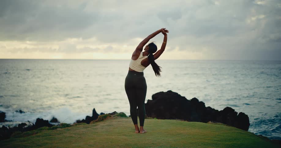 A graceful woman performs a series of yoga stretches on a lush green cliff with a stunning ocean view at sunrise