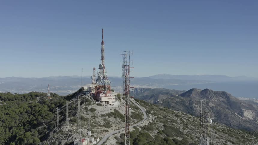 Aerial view of a telecommunication station with large antennas on a mountain summit overlooking the sea on a sunny day