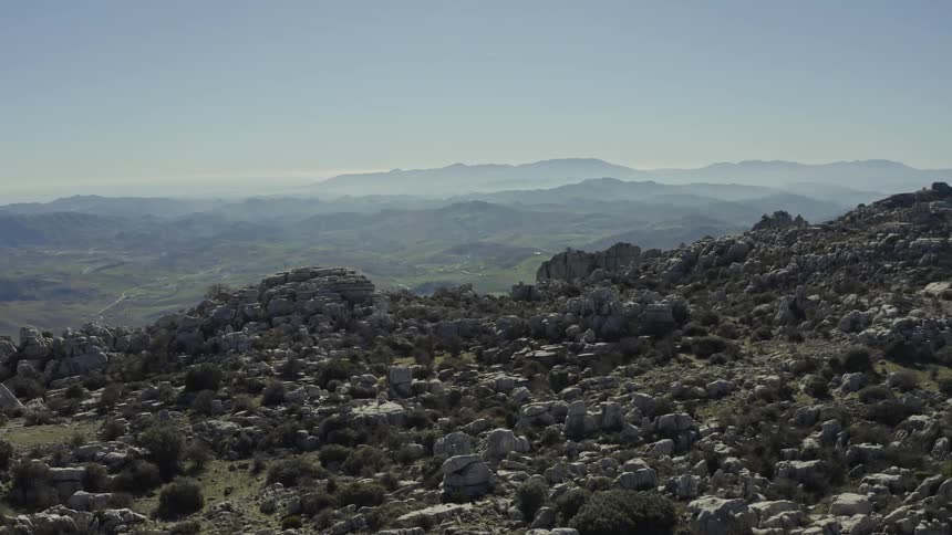 Expansive aerial view of a rugged, rocky mountain range overlooking a distant, hazy valley on a clear day