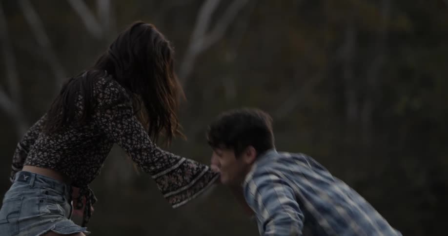 A woman helps a man climb upwards in a forested area