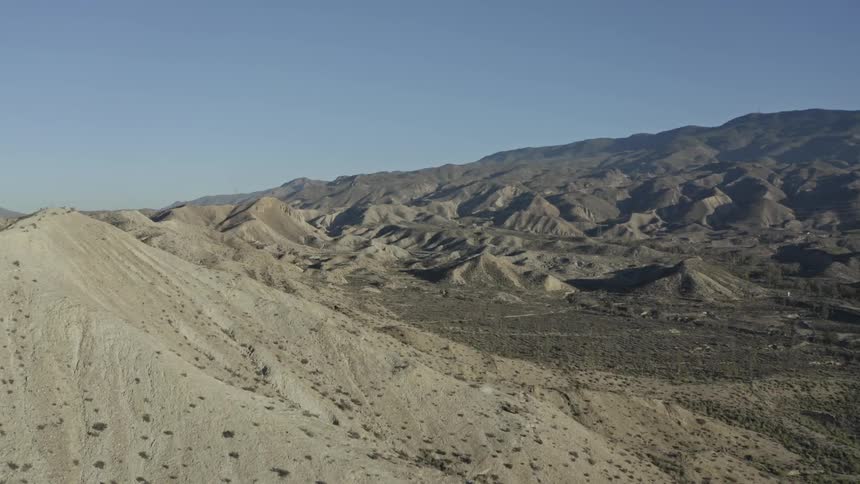 A stunning aerial view flies over the vast, arid badlands and mountains of a sun-baked desert
