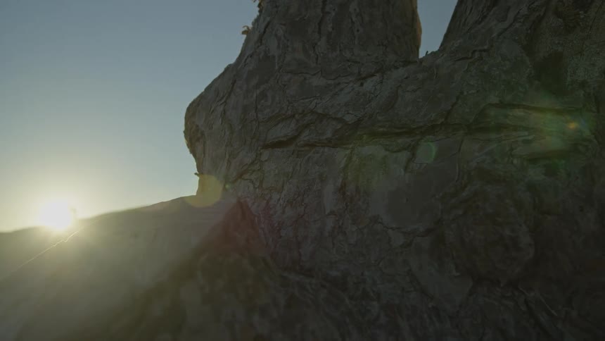 Close-up on a large rock as the sun rises in a time-lapse, revealing the silhouette of a person walking across the landscape