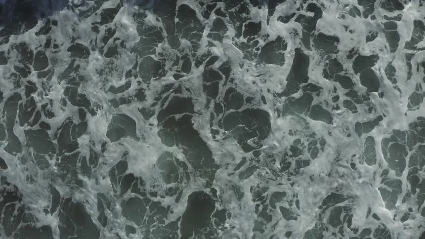 A dramatic top-down aerial view captures the mesmerizing power of the ocean as a large wave breaks in slow motion