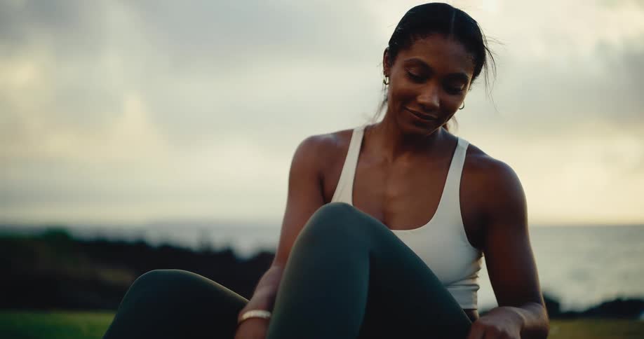 A beautiful and athletic woman peacefully prepares for her workout at sunset with the ocean in the background