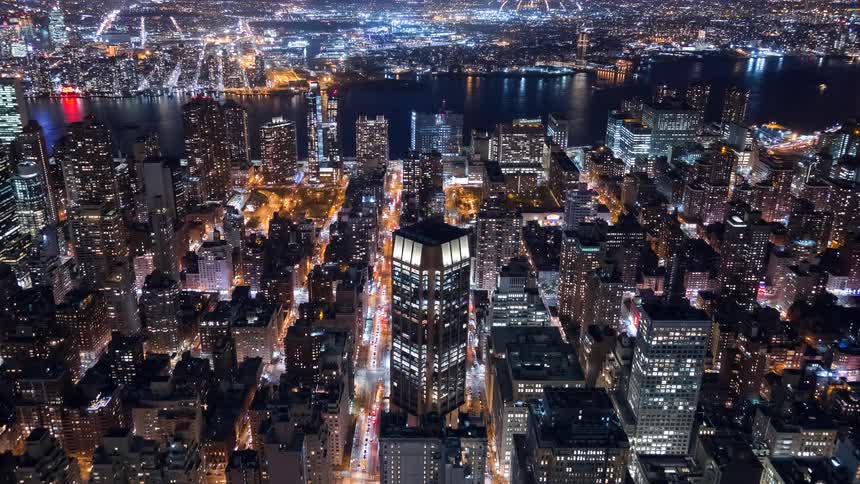 A stunning high-angle night timelapse captures the glittering lights of the New York City cityscape as traffic streams through the busy streets below