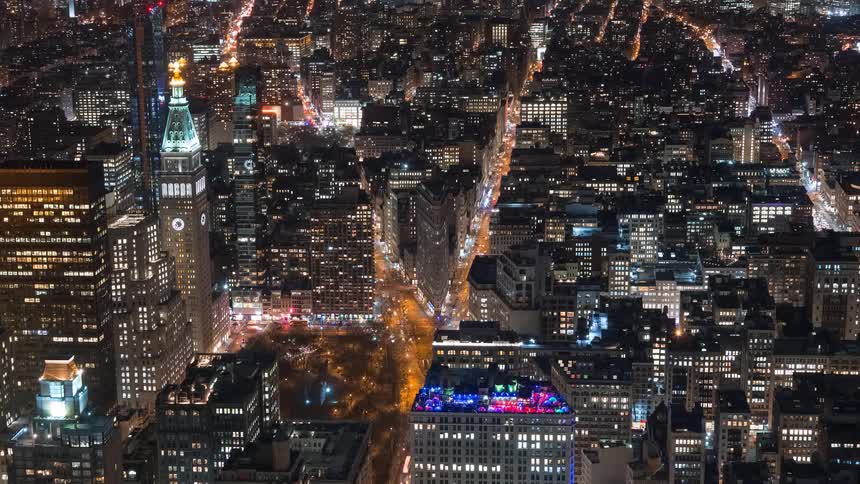A bustling time-lapse of New York City at night, with a high-angle view of the iconic Flatiron Building and the surrounding illuminated cityscape