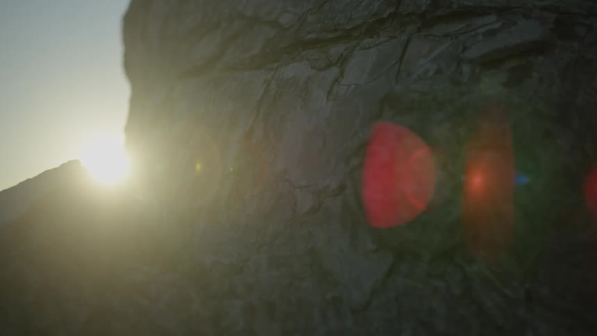 Close up of the sun emerging from behind a rugged rock face with a dramatic red lens flare