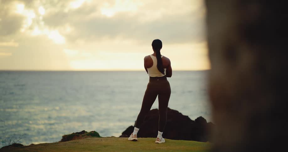 An athletic woman stands on a dramatic coastal cliff enjoying the beautiful sunrise over the ocean