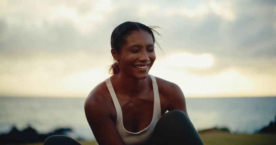 Portrait of a beautiful athletic woman laughing after her workout at sunset by the ocean