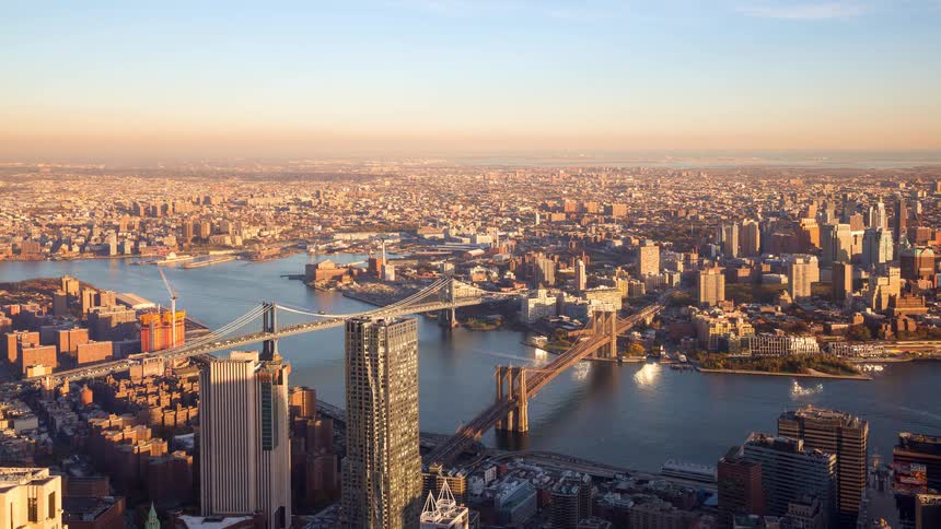 A stunning aerial timelapse captures traffic flowing over the Brooklyn and Manhattan Bridges in New York City as the sun sets over the sprawling cityscape