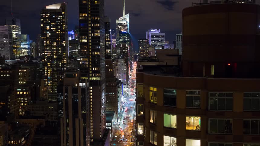 Time-lapse footage from a high angle shows the dazzling lights and fast-moving traffic on a busy New York City street at night