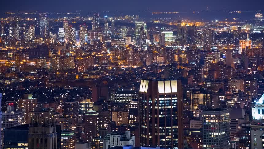 An aerial time-lapse view of the bustling New York City cityscape glowing with lights at night