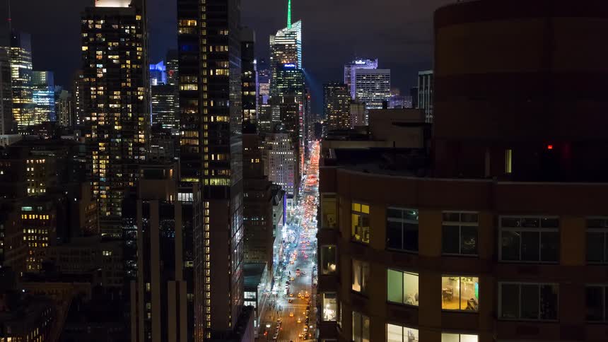 Nighttime timelapse of a busy New York City street with traffic flowing between illuminated skyscrapers