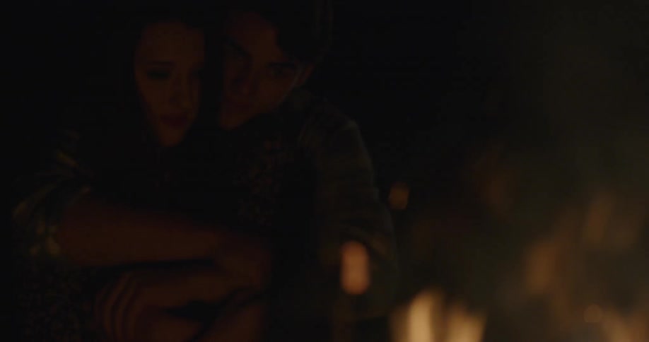 A man and woman cuddle next to a bonfire