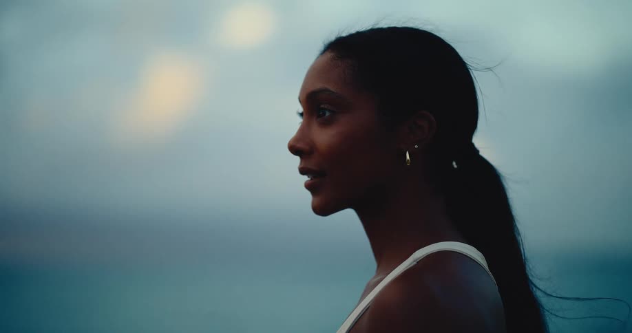 Close-up portrait of a serene young woman smiling gently as she looks out towards the ocean at dusk