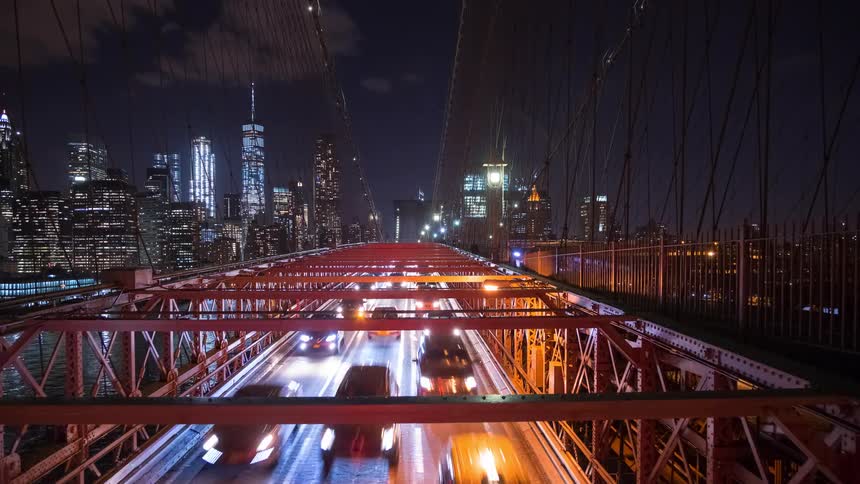 Night time-lapse of bustling traffic on the Brooklyn Bridge with the iconic illuminated Manhattan skyline in the background