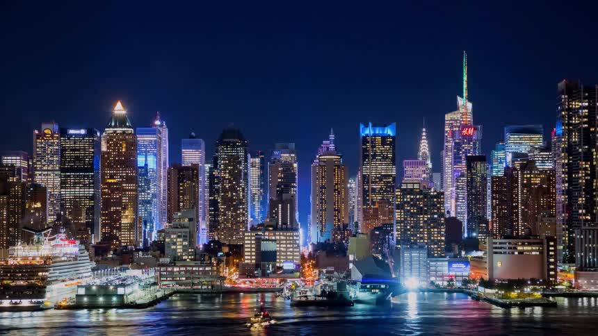A stunning panoramic view of the illuminated Midtown Manhattan skyline at night, showcasing iconic skyscrapers and the bustling Hudson River