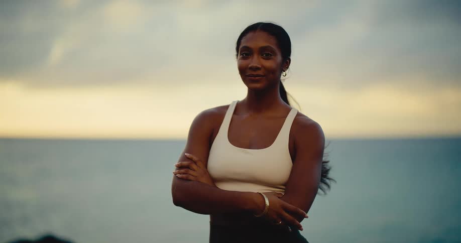 Portrait of a strong and confident athletic woman smiling at the camera with the ocean and sunset in the background