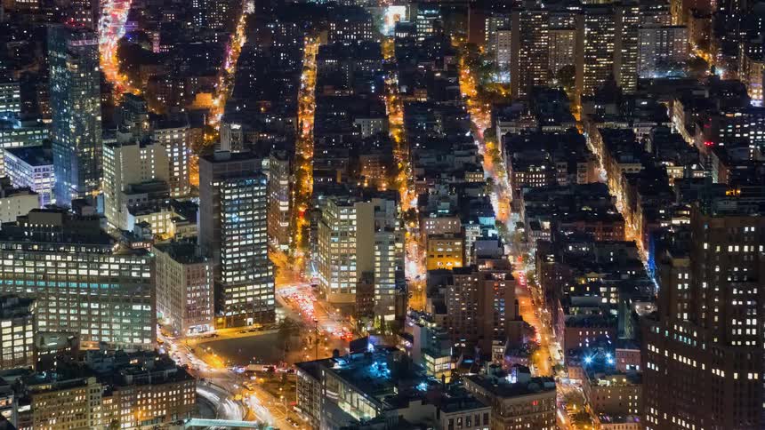 A mesmerizing high-angle time-lapse of New York City at night, showing streams of traffic lights flowing between illuminated skyscrapers