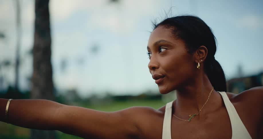 A beautiful and focused Black woman gracefully transitions through yoga poses in a peaceful outdoor park setting