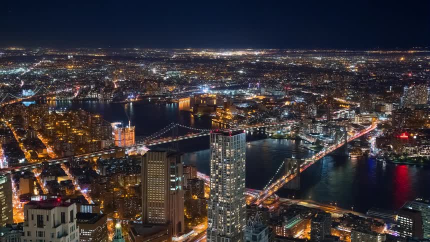 Stunning aerial time-lapse of the New York City skyline at night, with traffic flowing over the iconic Brooklyn and Manhattan Bridges