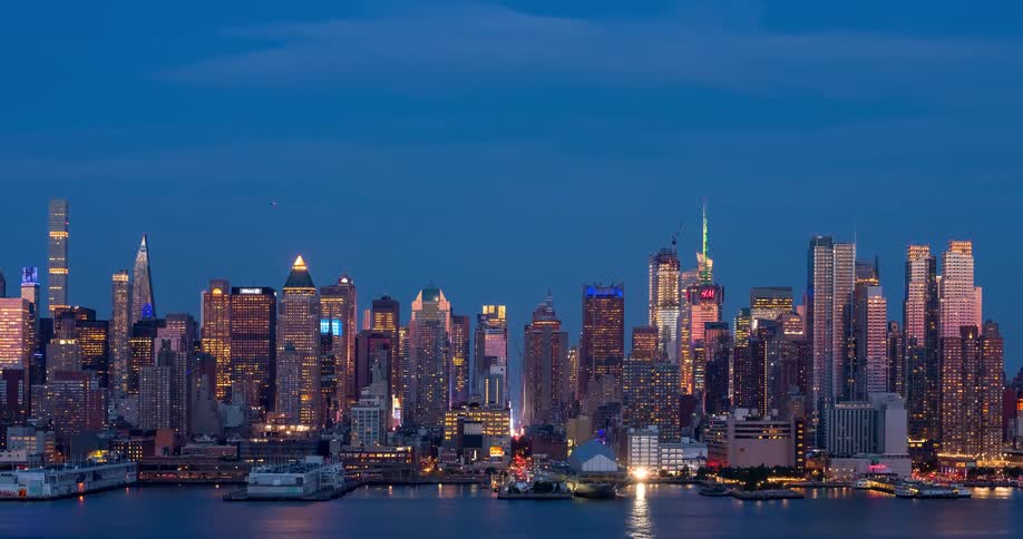 A beautiful time-lapse captures the iconic Midtown Manhattan skyline transitioning from dusk to night as vibrant city lights reflect on the water