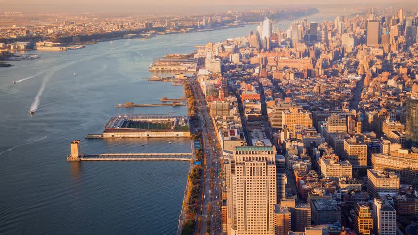 An aerial time-lapse captures the bustling West Side Highway and Hudson River in Manhattan as golden hour sunlight illuminates the city skyline