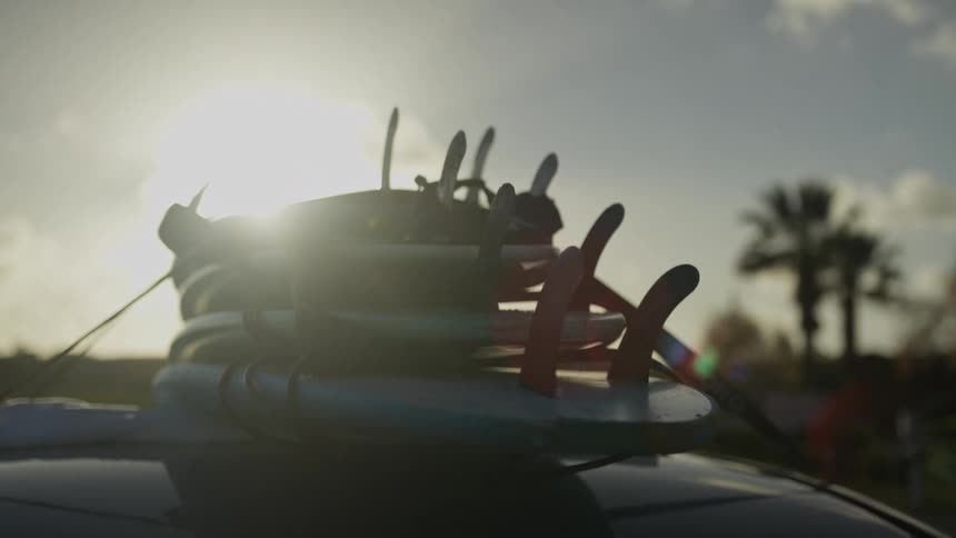 A close-up shot of surfboards strapped to the roof of a car, silhouetted against the bright afternoon sun