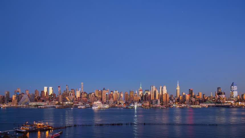 A stunning day-to-night time-lapse shows the iconic Midtown Manhattan skyline transitioning from a colorful sunset to a dazzling display of city lights