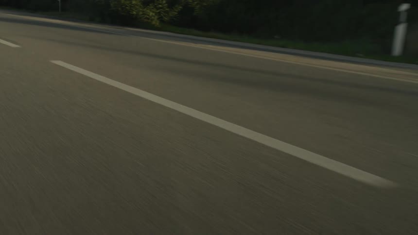 A fast point-of-view shot of a car speeding down an asphalt road during the golden hour