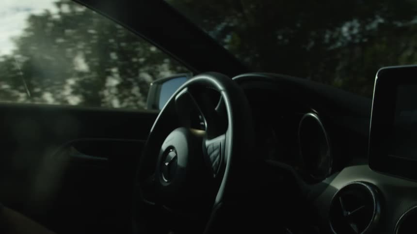 Slow motion shot from inside a car focusing on a person's hands on the steering wheel while driving along a scenic highway on a sunny day