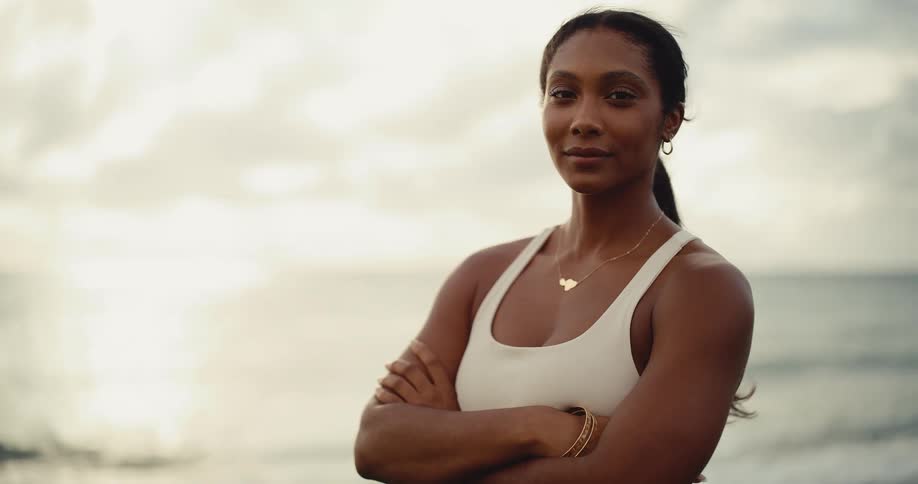 Portrait of a beautiful and confident athletic woman with her arms crossed looking into the camera on the beach at sunrise