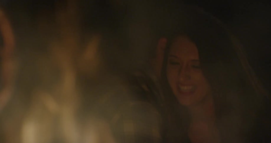 Man and woman laugh in front of a fire outside at night