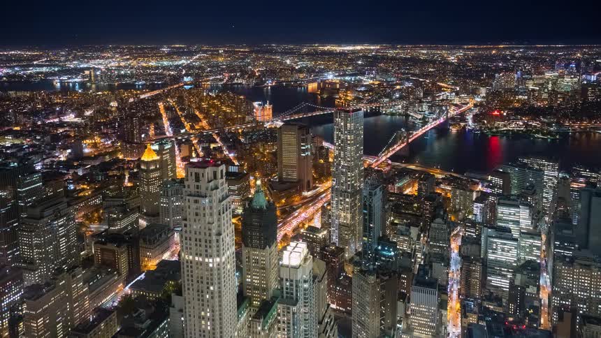 Expansive aerial time-lapse view of the vibrant New York City skyline and traffic flow at night