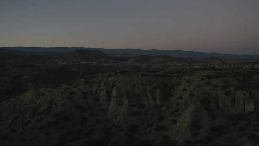 A static aerial view of a vast, rugged desert mountain range under a serene twilight sky