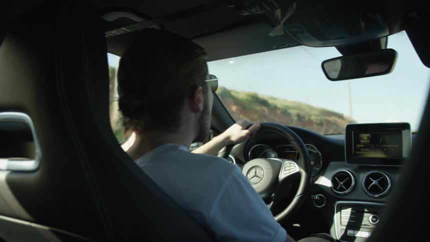 Rear view shot of a young man enjoying a drive in his car on a bright summer day