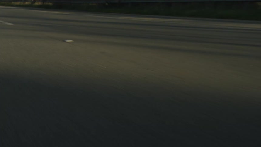 A low-angle, point-of-view shot captures the blur of asphalt and white lane markings from a speeding vehicle on a highway