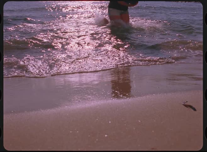 Vintage Super 8 footage shows a person running into the sparkling ocean waves to retrieve a ball