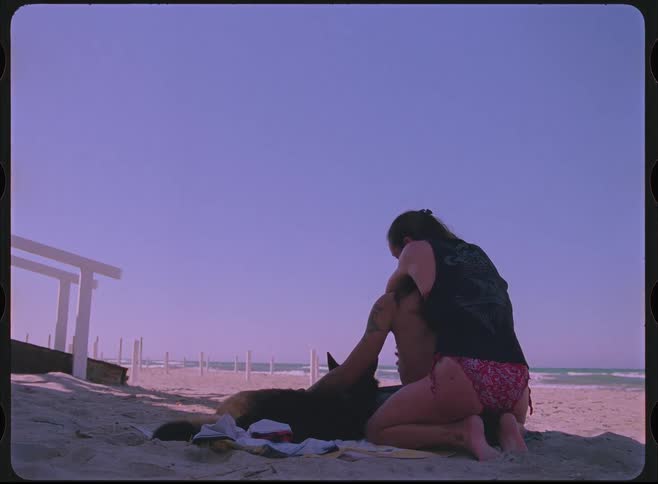 A vintage-style film captures a romantic couple and their dog relaxing and hugging on a sandy beach