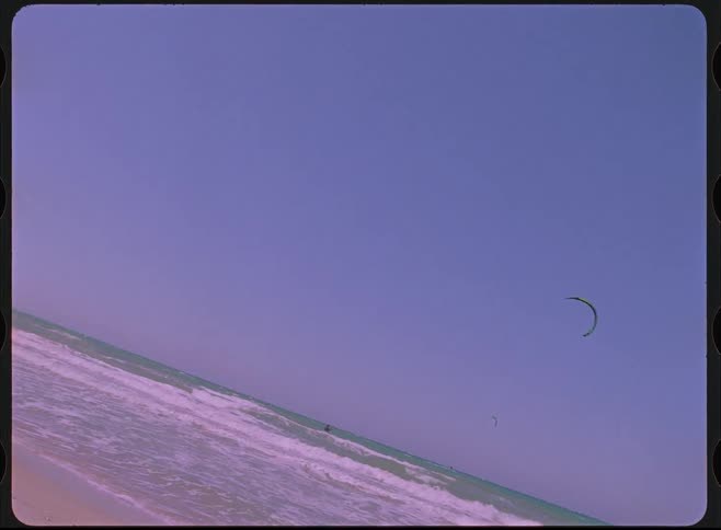 A Dutch angle shot of a kitesurfer at the beach captured on nostalgic, purple-hued film